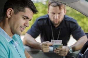 A man sits in the driver's seat of a car while a police officer stands outside, engaging in conversation