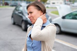 A woman standing on the street, holding her neck in discomfort, indicating pain or strain