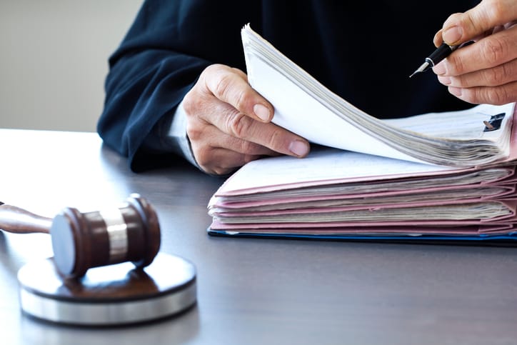 A judge in a black robe writes on a legal document with a pen